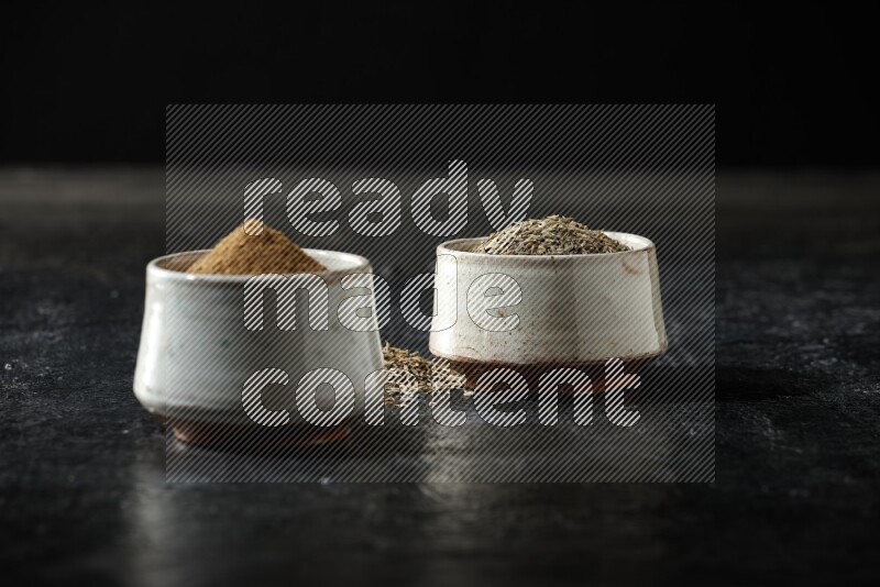 وعاءين بيج، أحدهما ممتلئ ببودرة الكمون والآخر ممتلئ بحبوب الكمون، على خلفية سوداء