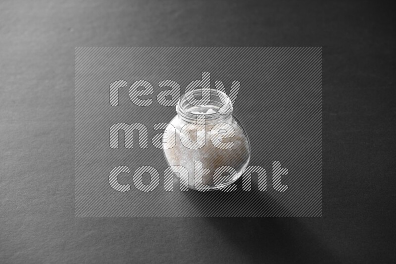 A glass spice jar full of salt on black flooring