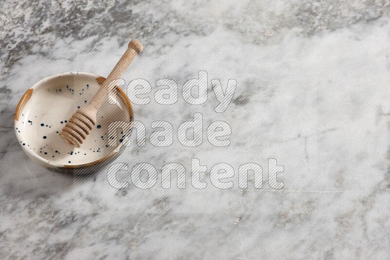 Multicolored pottery bowl with wooden honey dipper in it on grey marble background