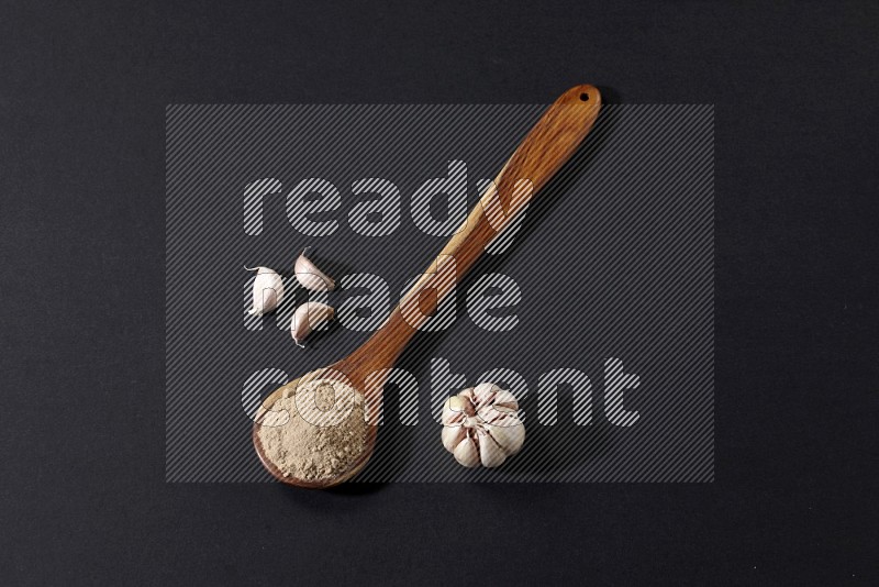 A wooden ladle full of garlic powder with garlic bulb and cloves beside it on a black flooring in different angles
