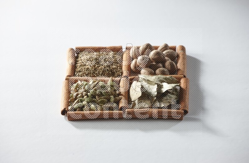 4 مربعات من أعواد القرفة ممتلئة بجوزة الطيب وأوراق الغار وحبوب الهيل والكمون على أرضية بيضاء