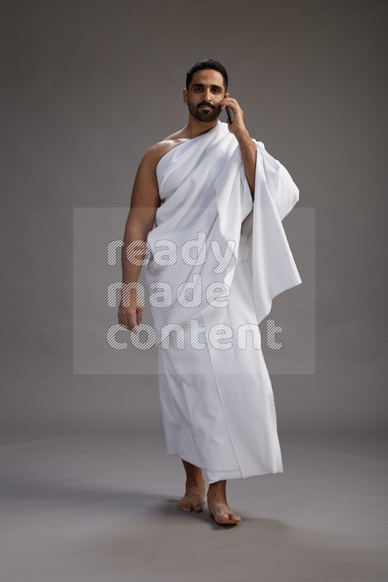 A man wearing Ehram Standing talking on phone on gray background