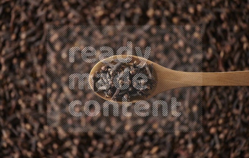 A wooden spoon full of cloves on cloves background and black flooring