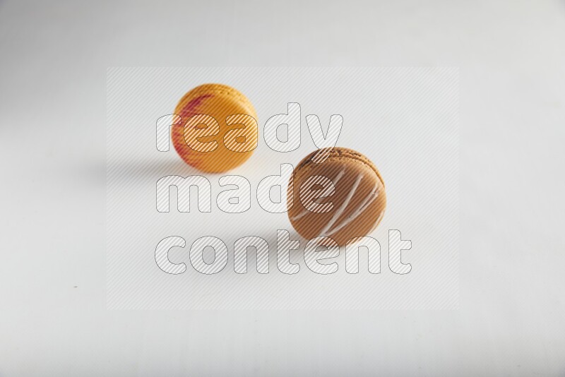 45º Shot of of two assorted Brown Irish Cream, and Orange Exotic macarons on white background