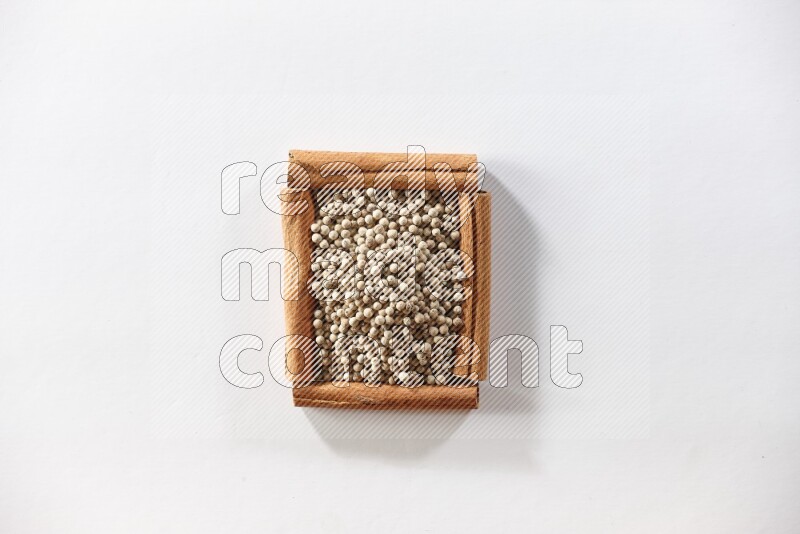 A single square of cinnamon sticks full of white pepper on white flooring