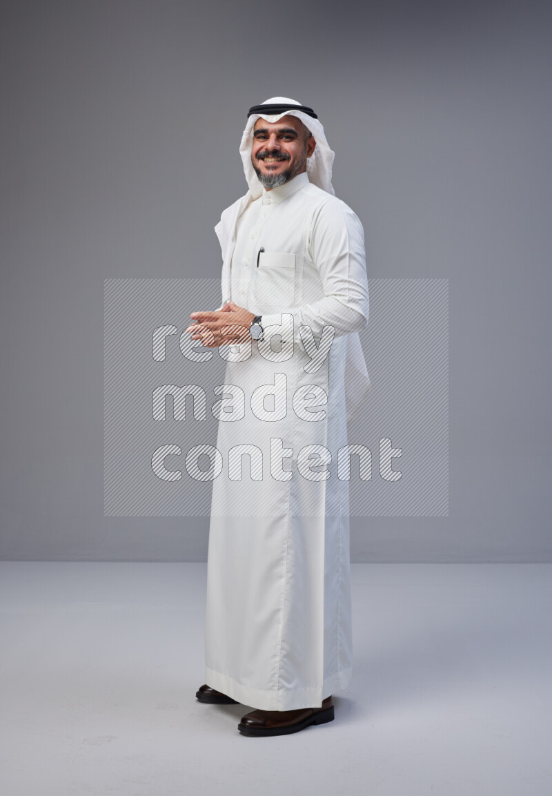 Saudi man Wearing Thob and white Shomag standing interacting with the camera on Gray background