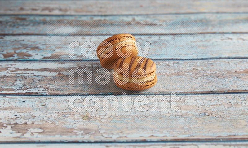 45º Shot of two light brown Almond Cream macarons on light blue wooden background