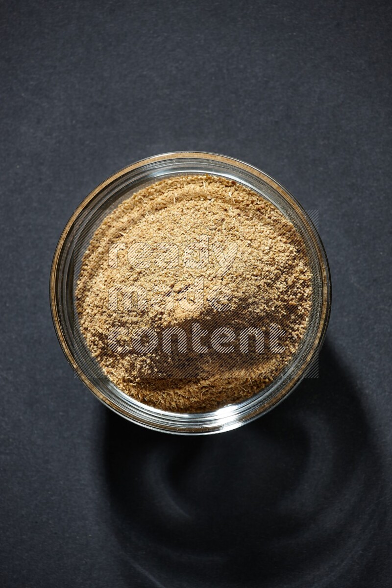 A glass bowl full of cumin powder on black flooring