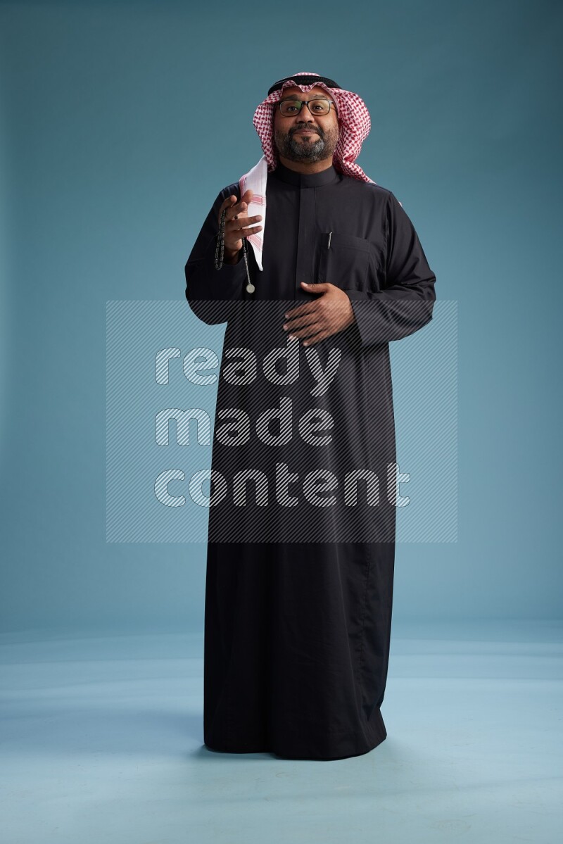 Saudi Man with shimag Standing Interacting with the camera on blue background
