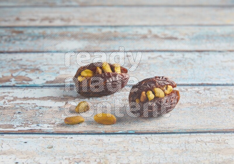 two pistachio stuffed madjoul dates on a light blue wooden background