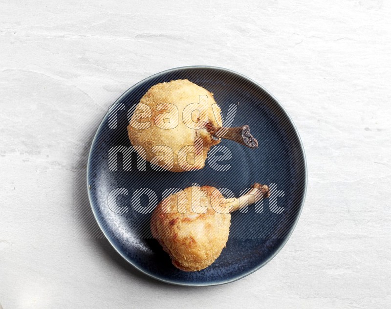 breaded drumstick on round dark grey pottery plate on grey textured countertop