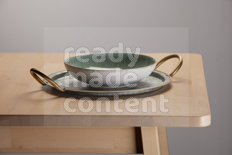 multicolored bowl placed on a rounded stainless steel tray with golden handels on the edge of wooden table