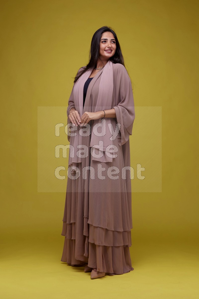 A woman Posing on a Yellow Background wearing Brown Abaya