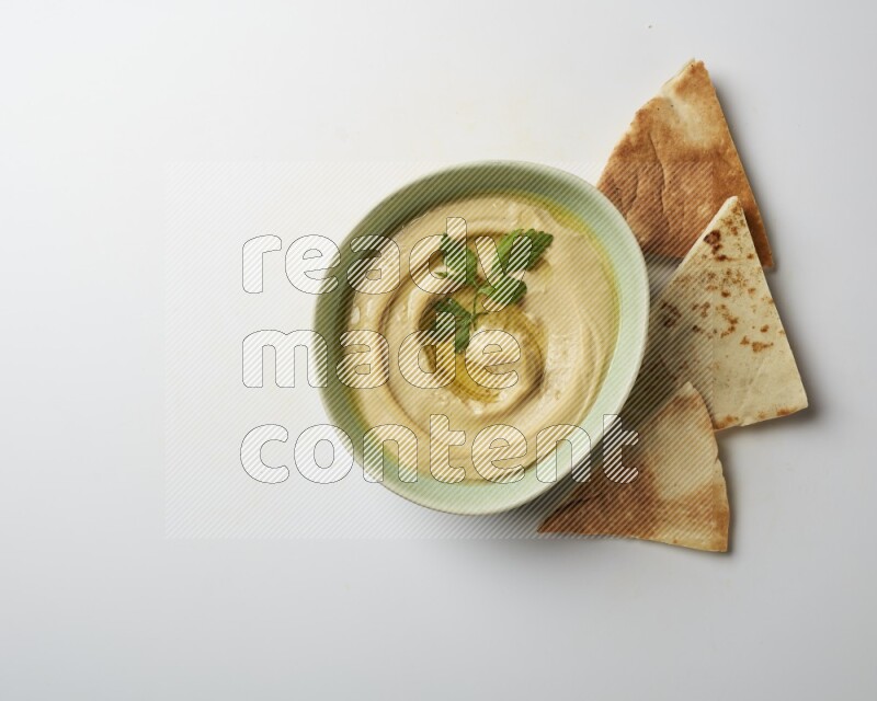 Hummus in a green plate garnished with parsley on a white background