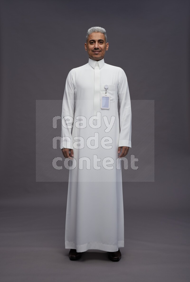 Saudi man wearing thob with pocket employee badge standing interacting with the camera on gray background