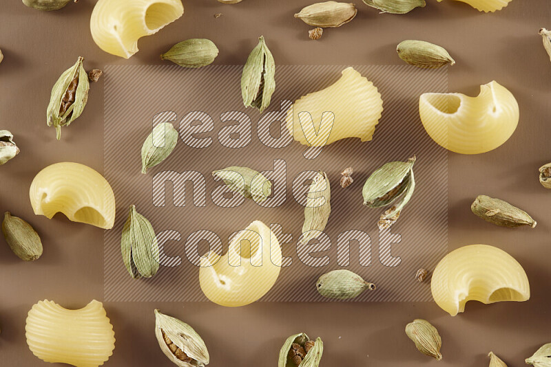 Raw pasta with different ingredients such as cherry tomatoes, garlic, onions, red chilis, black pepper, white pepper, bay laurel leaves, rosemary and cardamom on beige background