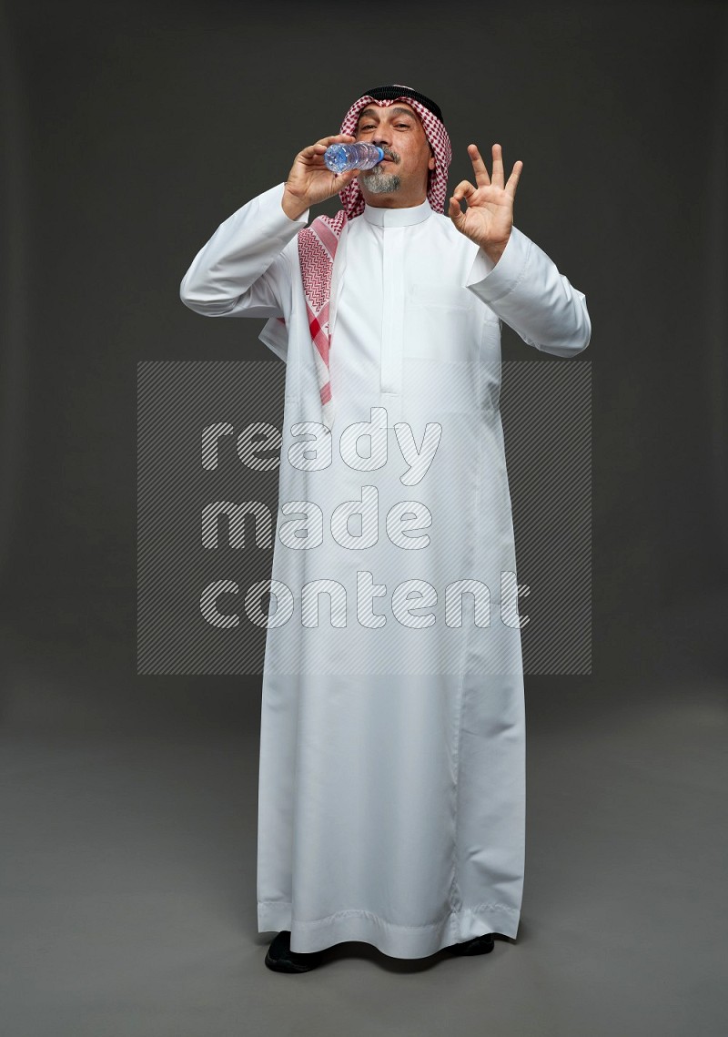 Saudi man with shomag Standing drinking water on gray background