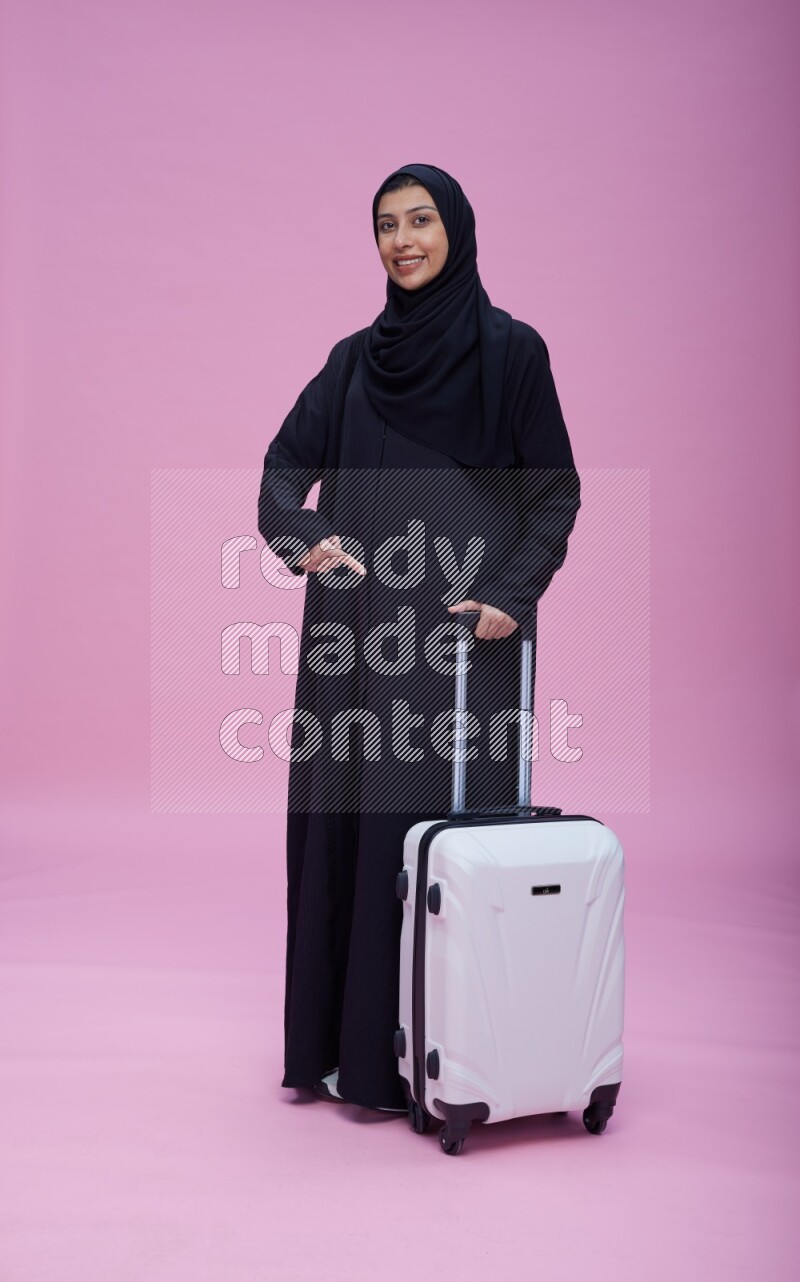 Saudi woman wearing Abaya standing holding bag on pink background