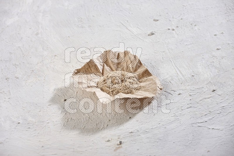 A crumpled piece of paper full of garlic powder on a textured white flooring in different angles