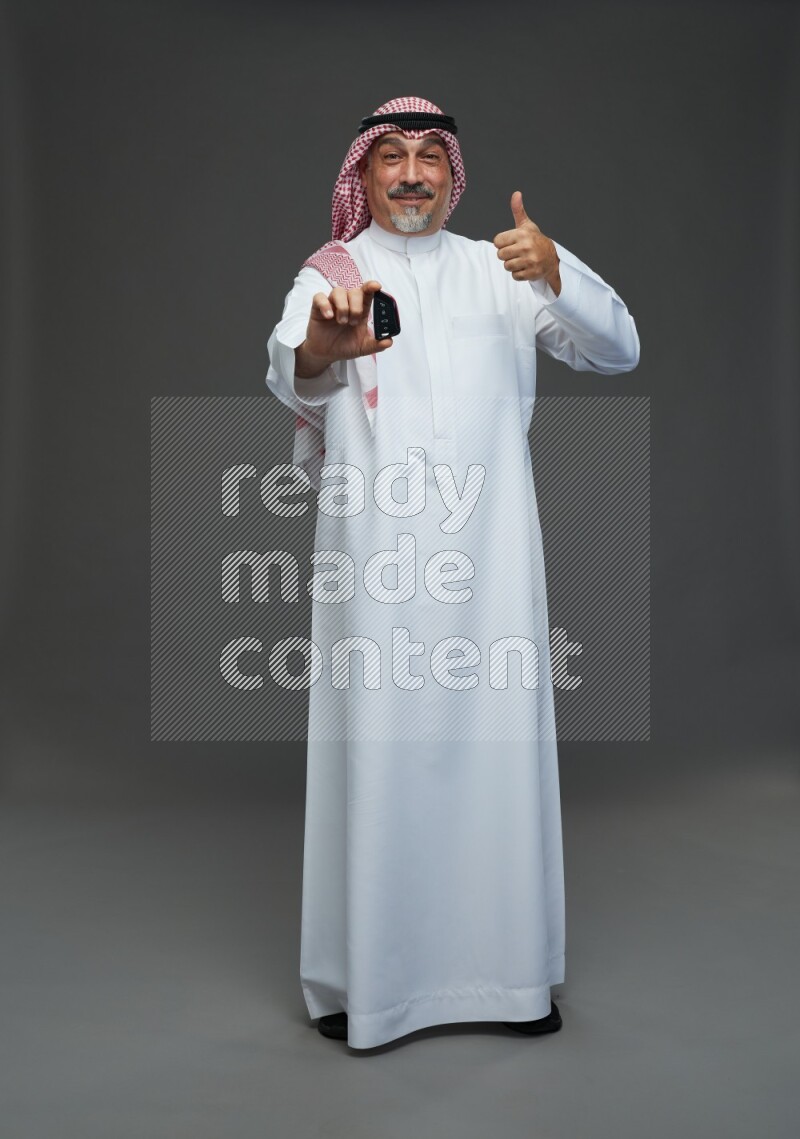 Saudi man with shomag Standing holding car key on gray background