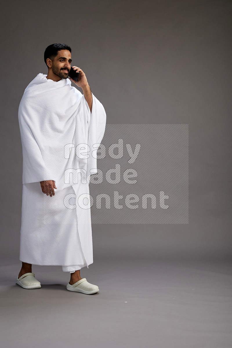 A man wearing Ehram Standing talking on phone on gray background