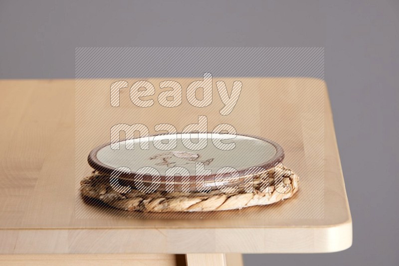 multi-colored pottery Plate placed on a small light colored straw placemat on the edge of wooden table