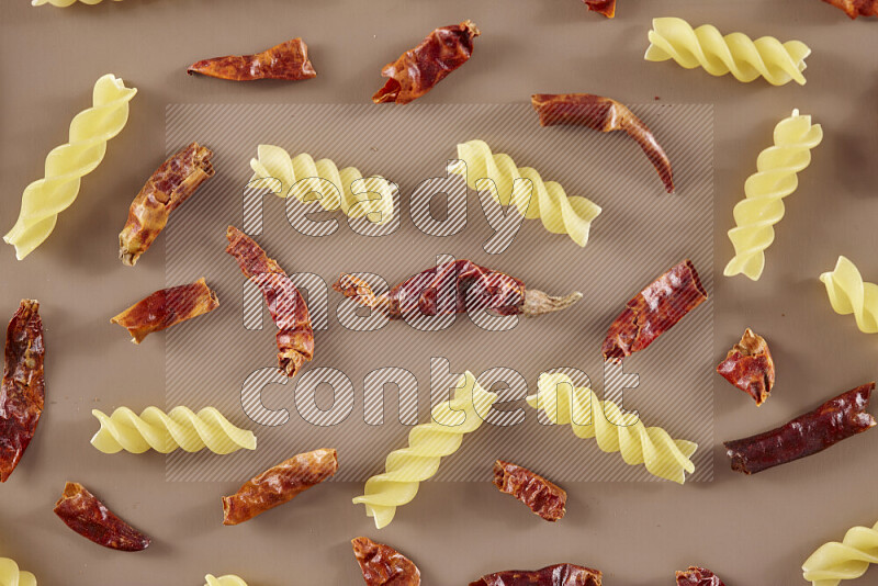 Raw pasta with different ingredients such as cherry tomatoes, garlic, onions, red chilis, black pepper, white pepper, bay laurel leaves, rosemary and cardamom on beige background