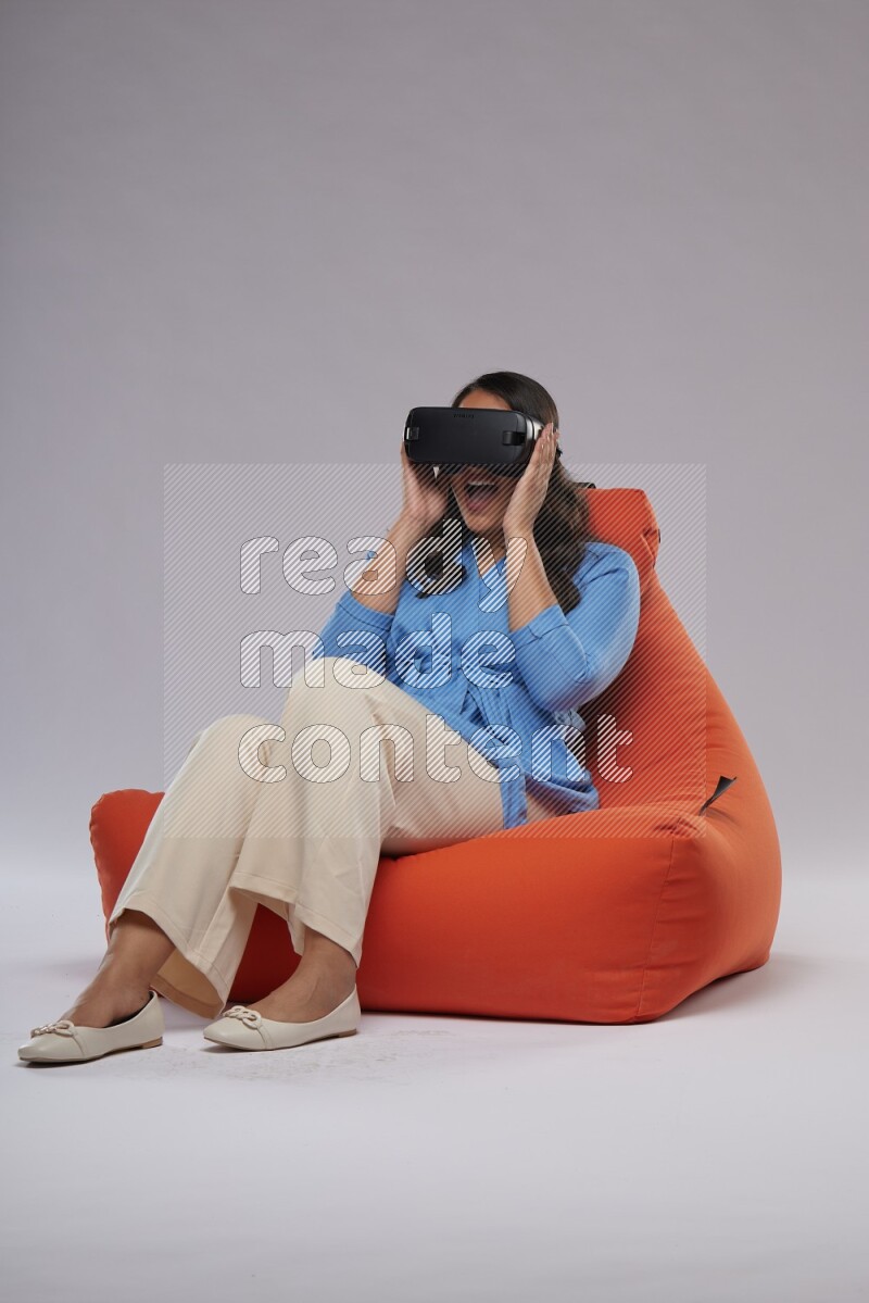 A woman sitting on an orange beanbag and gaming with VR