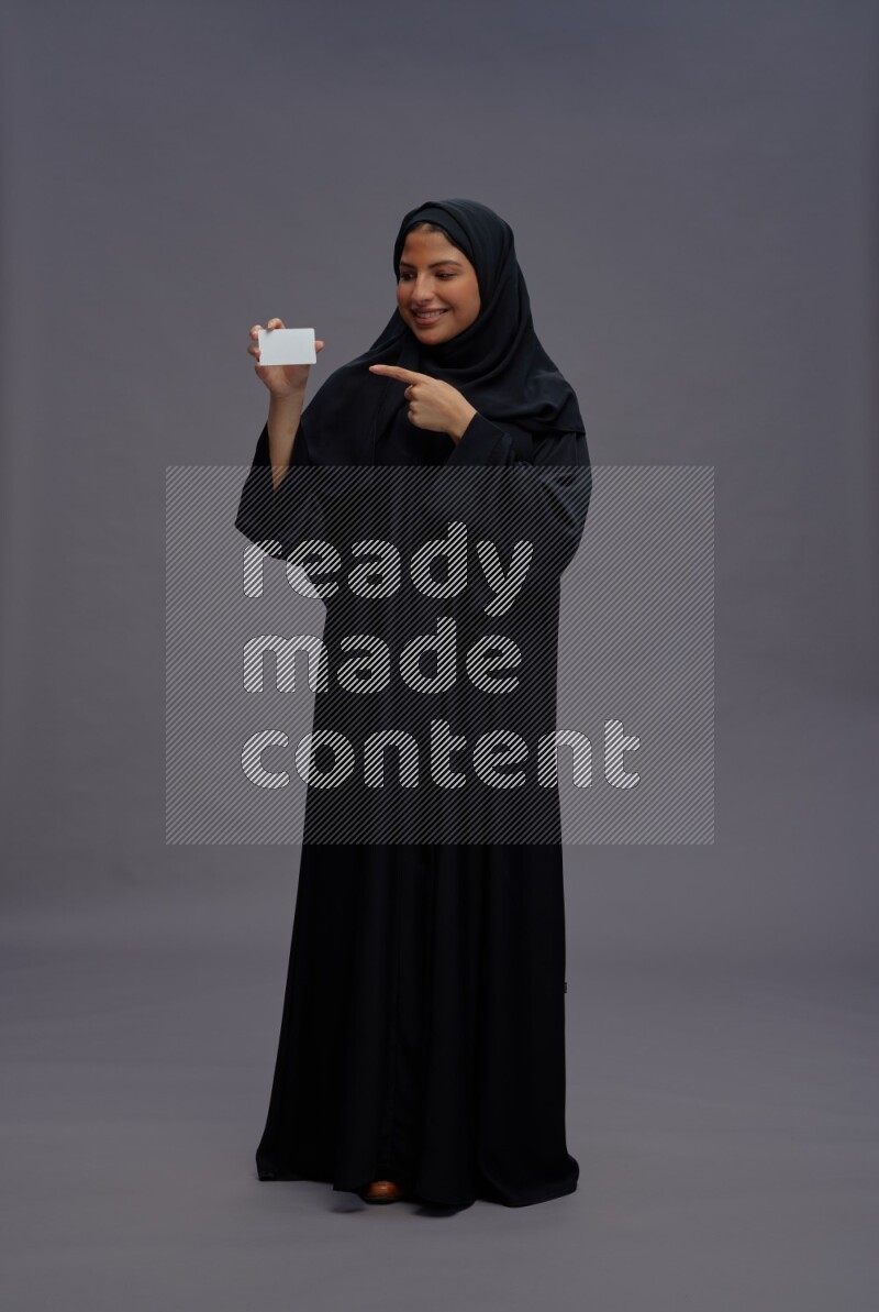 Saudi woman wearing Abaya standing holding ATM card on gray background
