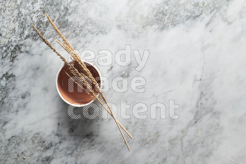 Wheat stalks on Brown Pottery Bowl on grey marble flooring, Top view