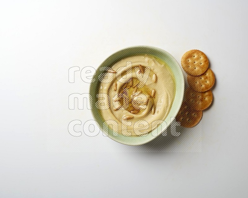 Hummus in a green plate garnished with pine nuts on a white background