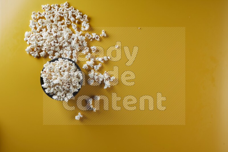A black ceramic bowl full of popcorn with popcorn beside it on a yellow background in different angles