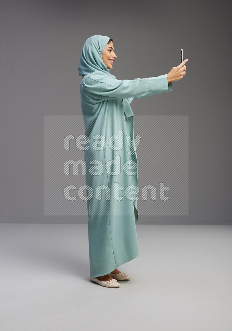 Saudi Woman wearing Abaya standing taking selfie on Gray background