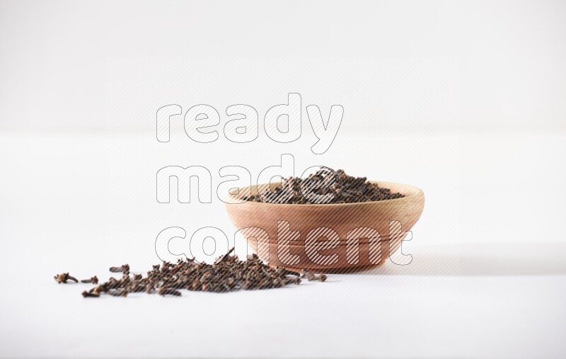 A wooden bowl full of cloves with spread grains on a white flooring
