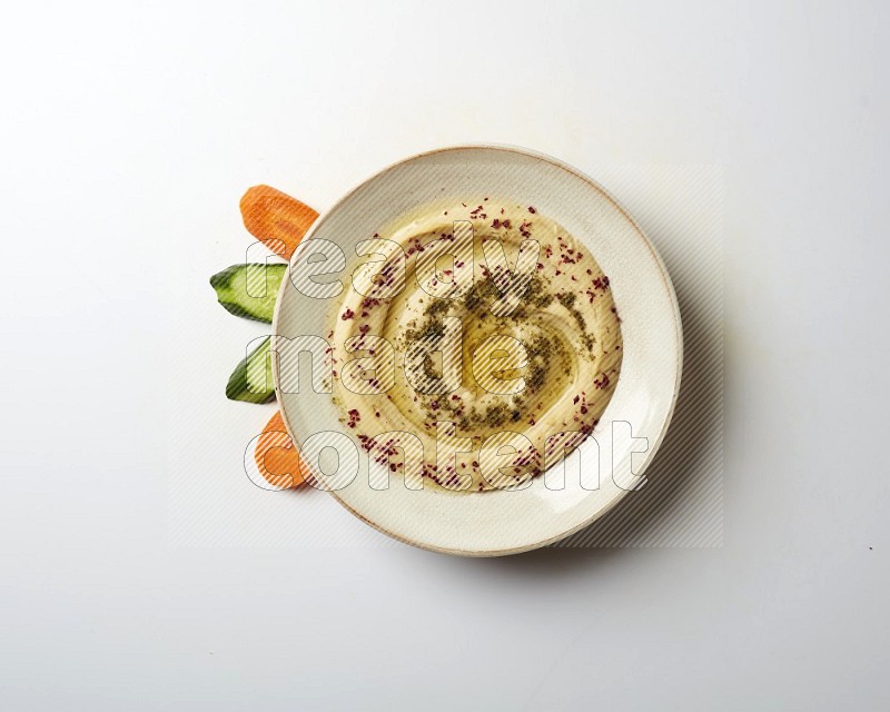 Hummus in a pottry plate garnished with zaatr & sumak on a white background