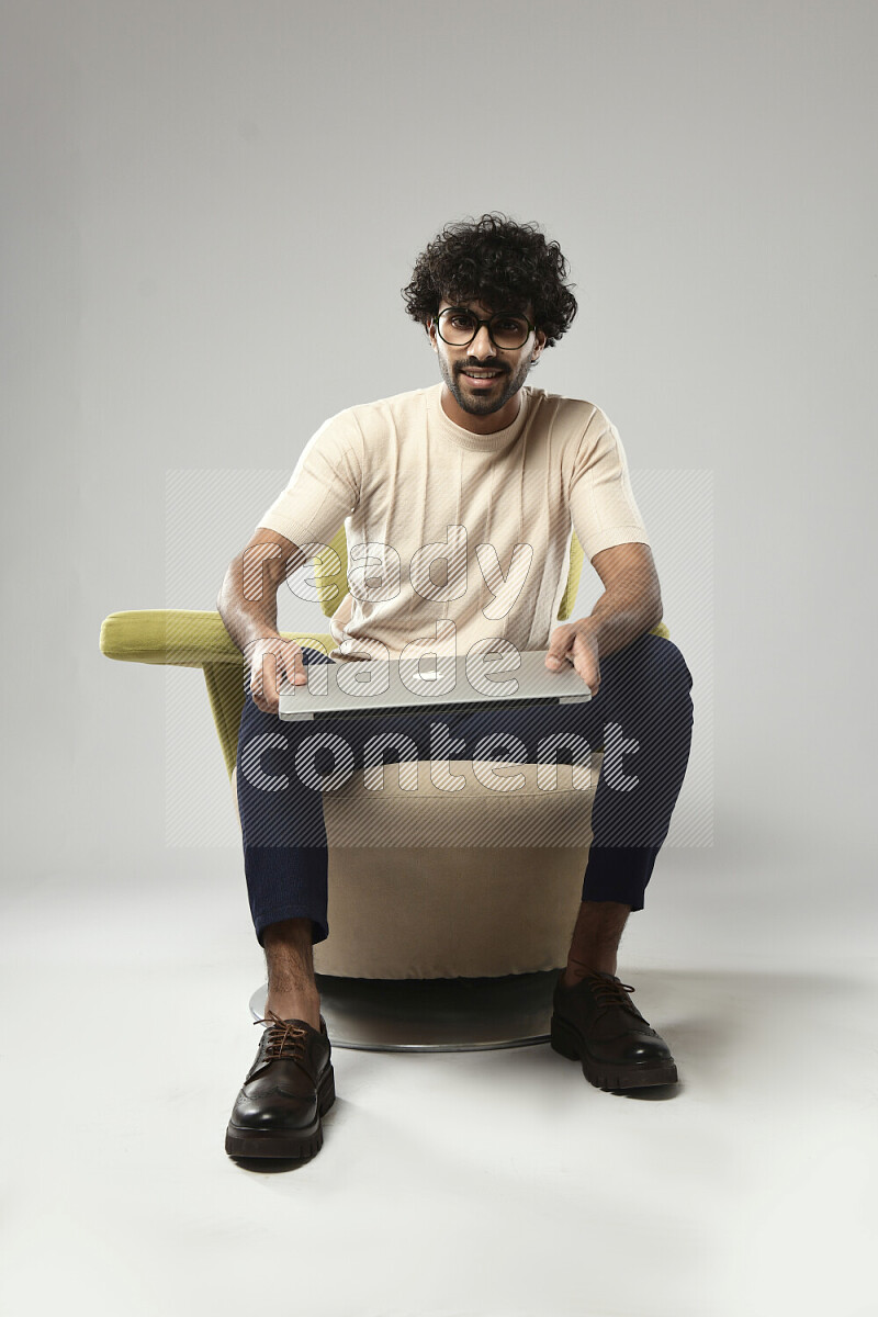 رجل يرتدي ملابس كاجوال يجلس علي كرسي و يحمل لاب توب علي خلفية بيضاء