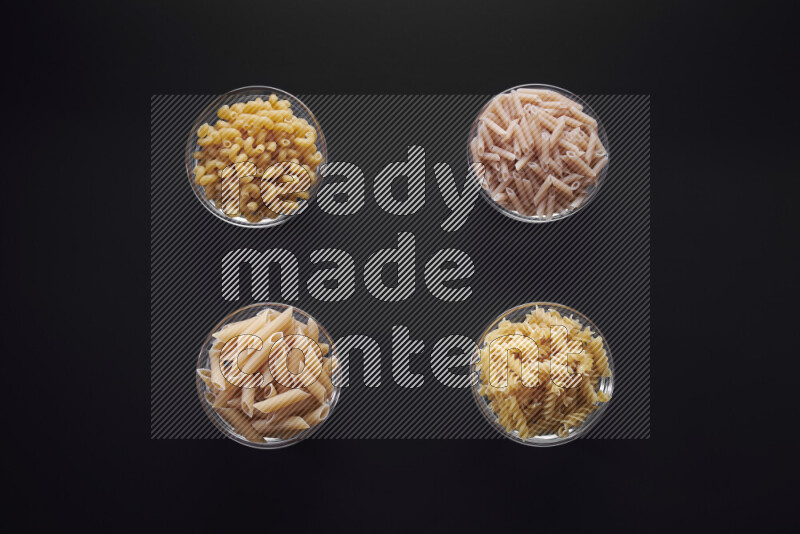 Different pasta types in glass bowls on black background