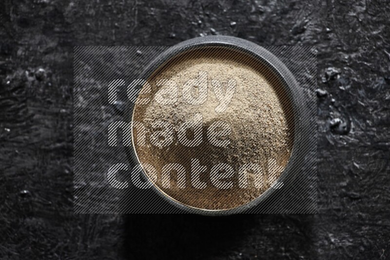 وعاء فخار أسود مملوء ببودرة الفلفل الأبيض على أرضية سوداء