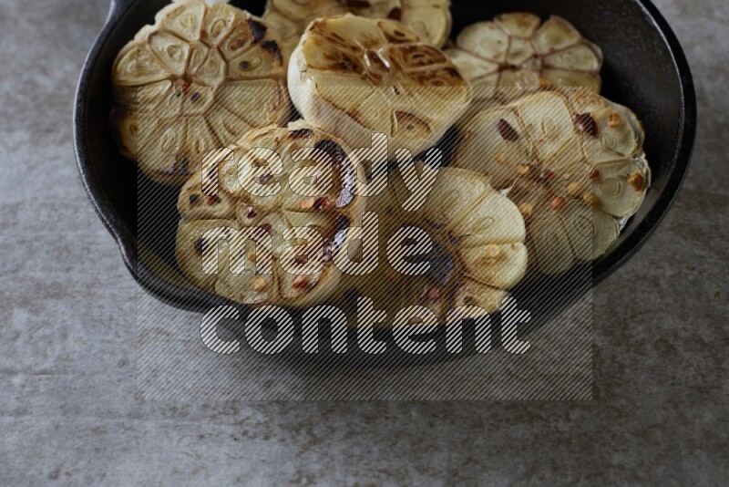 half's roasted garlic in a black pan on a grey textured countertop