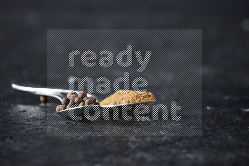 ملعقتان معدنيتان ممتلئتان ببودرة بهار الفلفل الحلو وحبوبه على خلفية سوداء