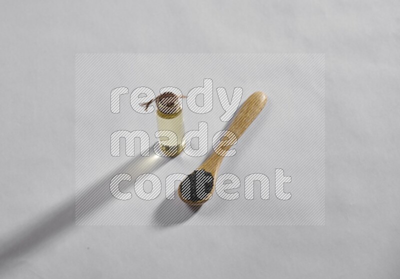 ملعقة خشبية ممتلئة ببذور حبة البركة مع زجاجة من زيت حبة البركة على أرضية بيضاء