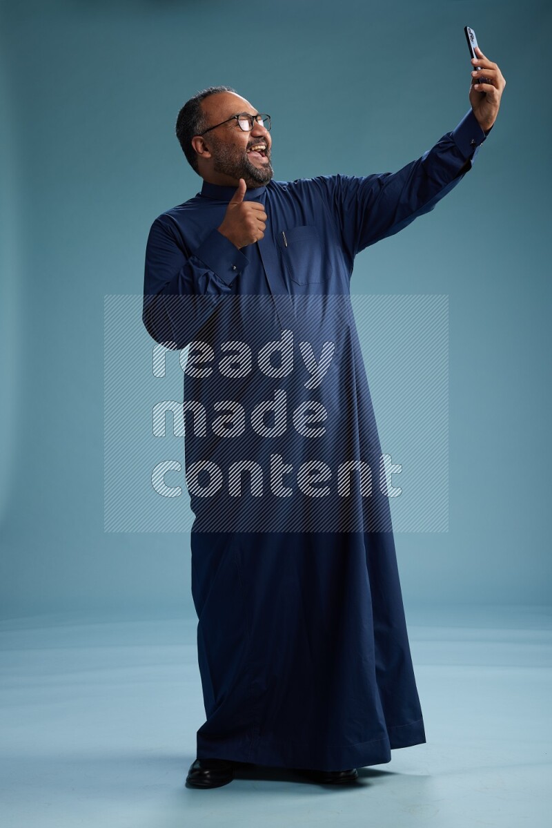 Saudi Man without shimag Standing taking selfie on blue background