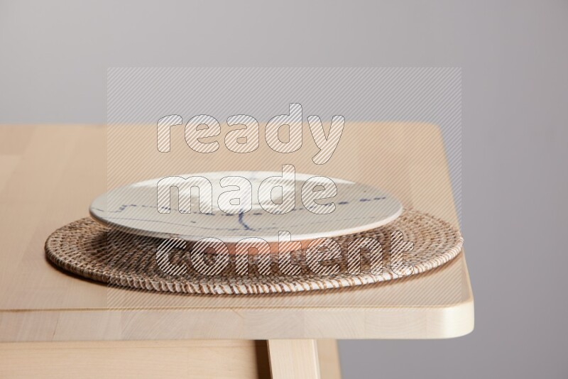 multi-colored pottery Plate placed on a big light colored straw placemat on the edge of wooden table