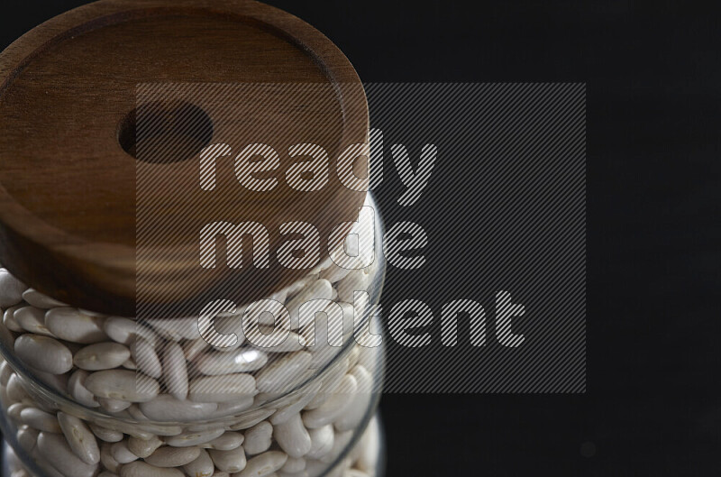 White beans in a glass jar on black background