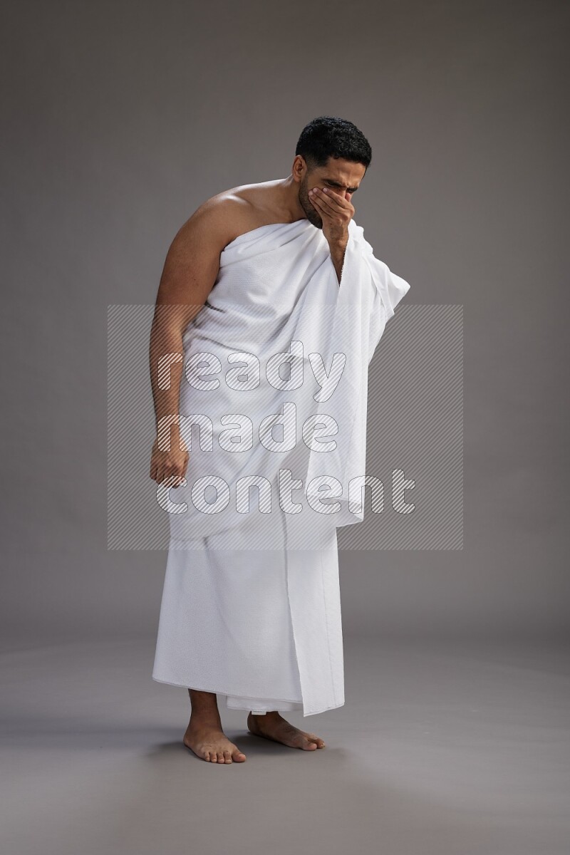 A man wearing Ehram standing showing how to sneeze on gray background