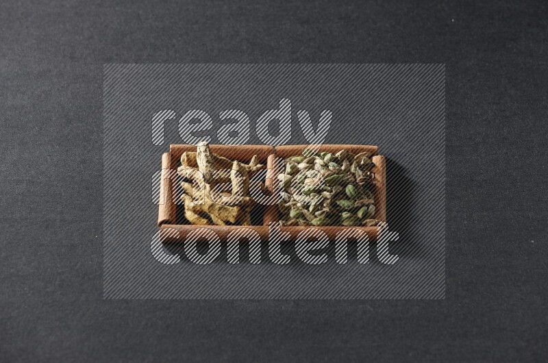 مربعان من أعواد القرفة ممتلئان بحبوب الهيل وأصابع الكركم علي خلفية سوداء