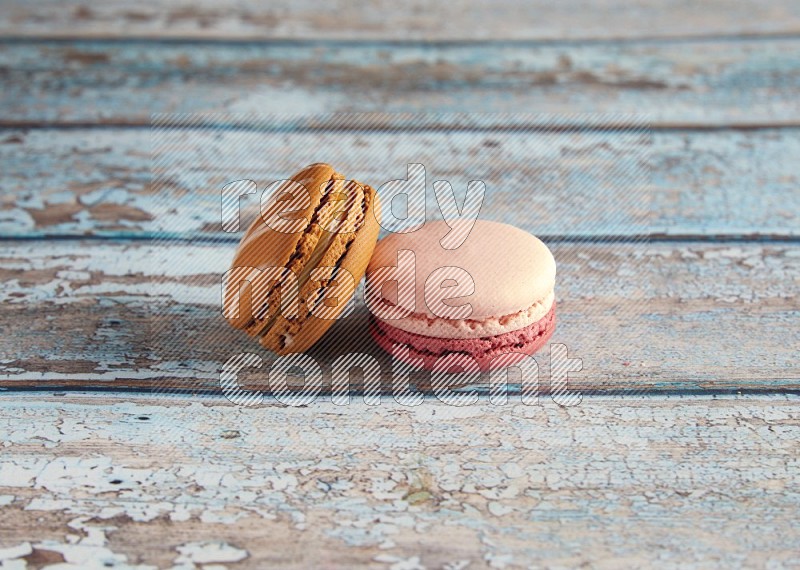 45º Shot of of two assorted Brown Irish Cream, and Pink Litchi Raspberry macarons on light blue background