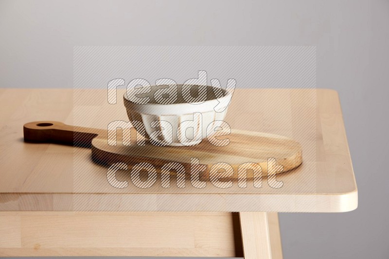 off white bowl placed on a  wooden oval cutting board on the edge of wooden table