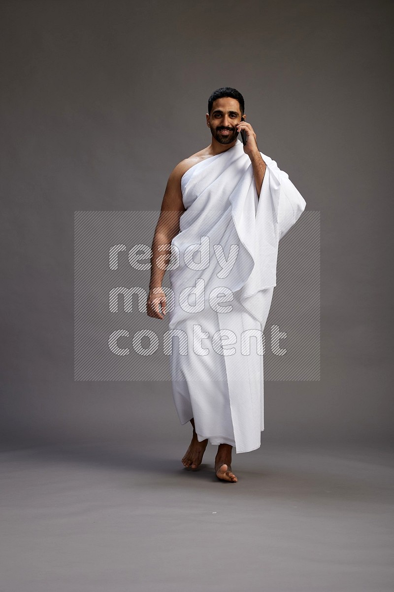 A man wearing Ehram Standing talking on phone on gray background