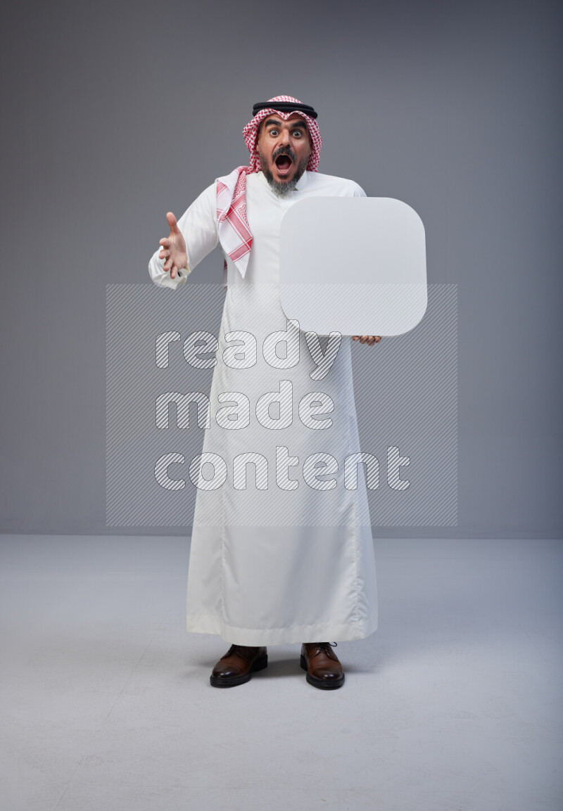 Saudi man Wearing Thob and red Shomag standing holding social media sign on Gray background